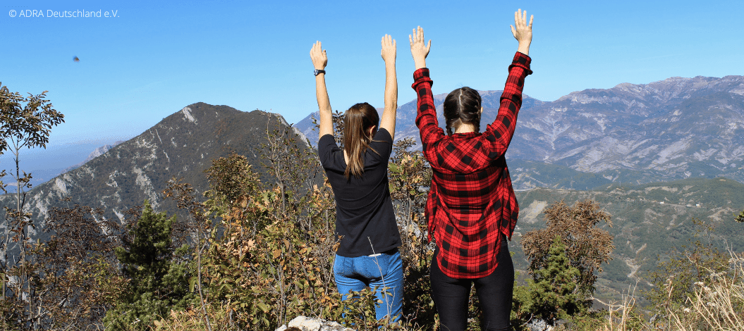 Ellen in Albanien genießt die atemberaubende Aussicht ihres Freiwilligendienstes in Albanien, mit ausgestreckten Armen zum Himmel, umgeben von malerischen Bergen und Landschaft.