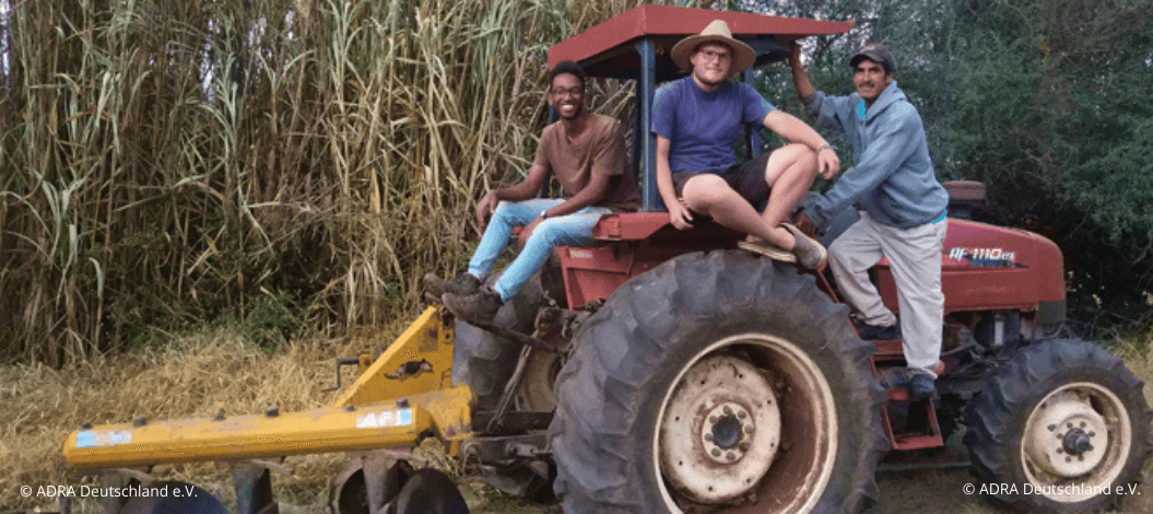 Dominik sitzt mit zwei Einheimischen auf einem Traktor in Bolivien.