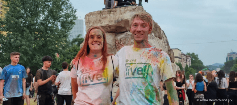 Freiwilliger während eines FSJ in Albanien beim Holy Color Festival mit ADRAlive!-Shirts, voller Farbe im Gesicht und auf der Kleidung