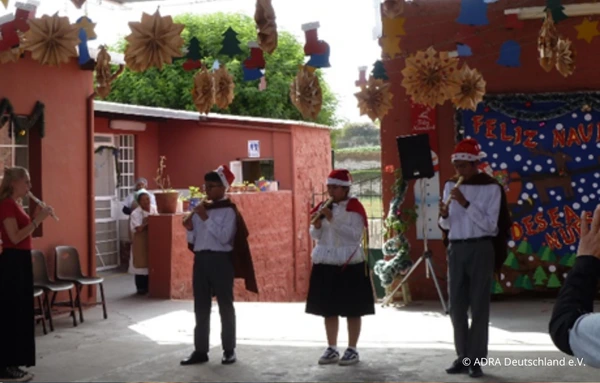 Kinder in Peru führen ein Weihnachtslied mit Flöten in einem festlich geschmückten Hof bei Nuestro Hogar auf.