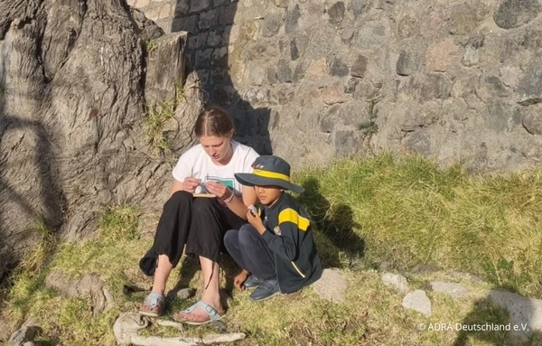 ADRAlive!-Freiwillige sitzt mit einem Jungen auf einer Wiese und liest oder bastelt mit ihm.