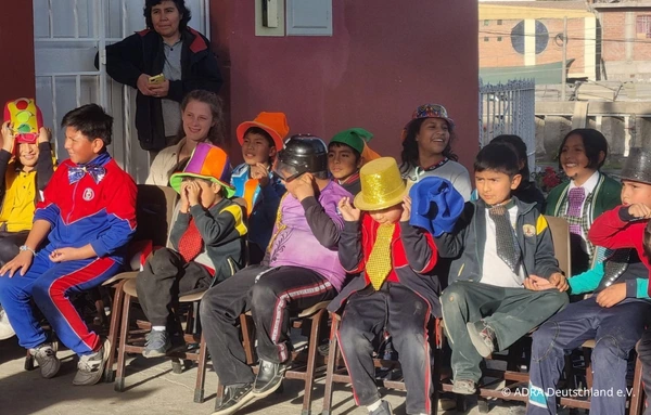 Kinder sitzen verkleidet mit bunten Hüten und Krawatten auf Stühlen bei einer Schulaufführung bei Nuestro Hogar in Peru