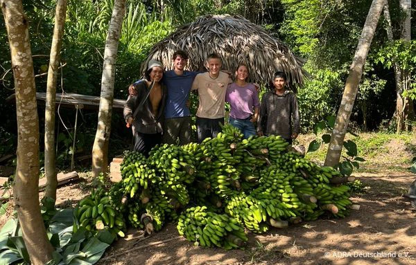 Eine Gruppe steht hinter einer großen Ernte grüner Bananen inmitten tropischer Vegetation