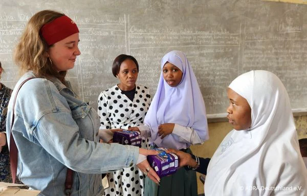 Eine Freiwillige überreicht einer Schülerin Menstruationsprodukte im Rahmen eines CWCD-Projekts an einer Schule in Arusha