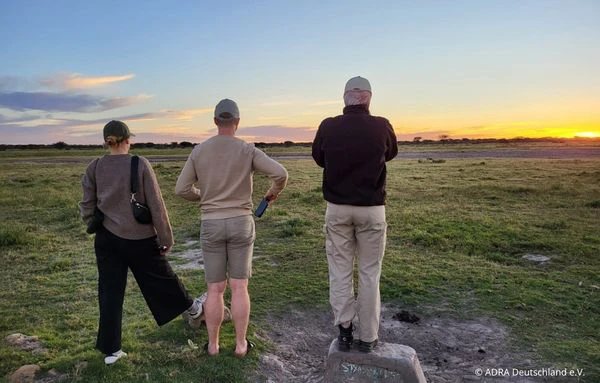 Drei Personen beobachten gemeinsam den Sonnenuntergang über einer weiten Landschaft in Mosambik