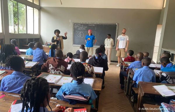 Freiwillige und Mitarbeitende sprechen in einem Klassenzimmer in Maputo mit Schülerinnen und Schülern über Umweltthemen