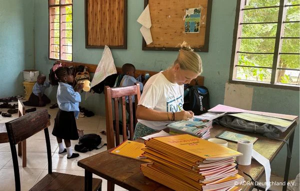 Freiwillige bereitet in einem Klassenraum von The Baobab Home Lern- und Unterrichtsmaterialien vor, während Kinder im Hintergrund zu sehen sind