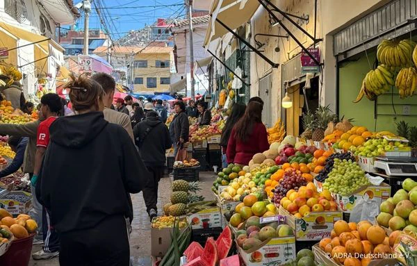 Blick durch eine belebte Marktgasse mit zahlreichen Ständen voller Obst und Gemüse