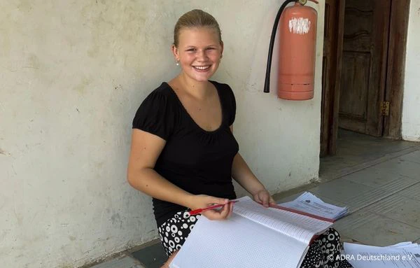 Freiwillige sitzt mit einem Ordner und Unterlagen auf dem Schulgelände von The Baobab Home in Bagamoyo