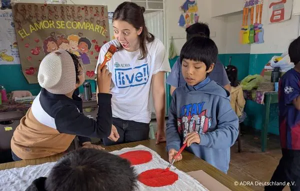Eine ADRAlive!-Freiwillige bemalt gemeinsam mit Kindern ein Spieltuch mit bunten Kreisen
