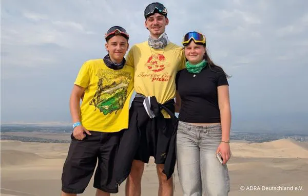 Drei junge Freiwillige stehen gemeinsam auf einer Sanddüne in Peru