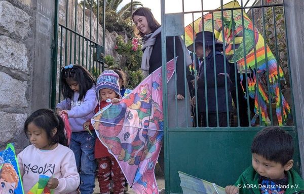 Eine Freiwillige begleitet mehrere Kinder mit bunten Drachen am Eingang eines Parks in Arequipa