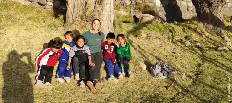 ADRA-Freiwillige sitzt mit fünf Kindern der Kindertagesstätte Nuestro Hogar im Freien in Arequipa, Peru
