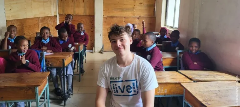 Ein ADRAlive!-Freiwilliger sitzt mit Schulkindern in einem Klassenzimmer der Albehije Primary School in Arusha, Tansania