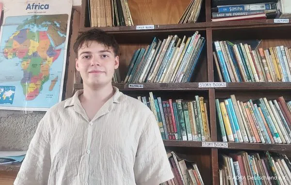 Ein ADRAlive!-Freiwilliger steht vor Bücherregalen in der Bibliothek der Albehije Primary School in Tansania