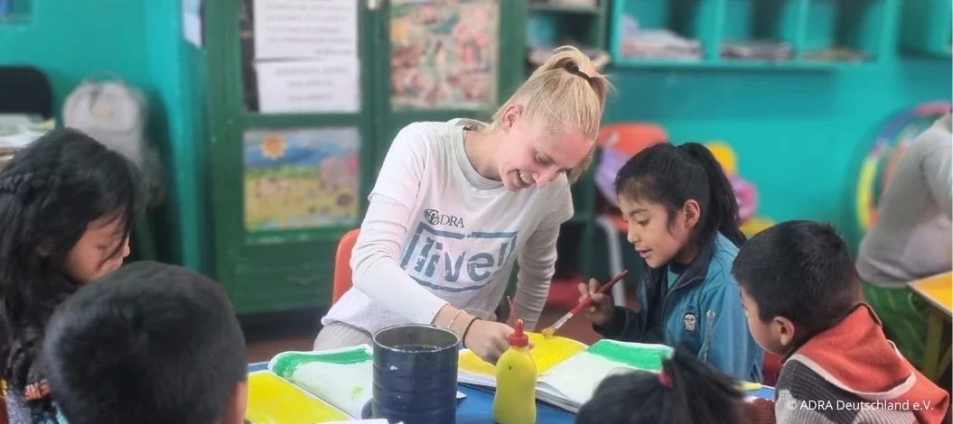 Header_Erfahrungsbericht_Alegra_in_Peru ADRAlive!-Freiwillige malt gemeinsam mit Kindern in einem bunt eingerichteten Klassenraum.