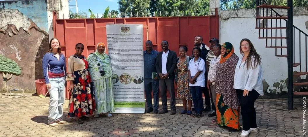 Gruppenfoto von Mitarbeitenden und Freiwilligen des Centre for Women, Children and Youth Development (CWCD) in Arusha vor dem Eingang der Organisation